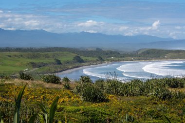 Sahilde dalgaların dalgalandığı, yemyeşil tepeler ve dağlarla çevrili, kumlu bir sahile vuran manzaralı bir sahil manzarası..