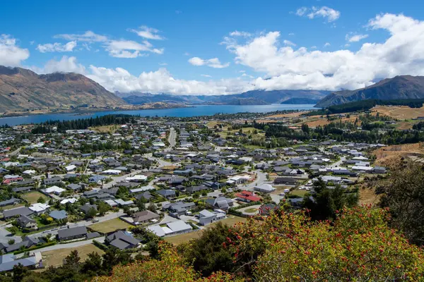 Dağlar ve göl arasında yuva yapmış panoramik bir kasaba. Modern evleri, yeşil manzaraları ve tüylü bulutları olan berrak mavi bir gökyüzü olan yerleşim alanları..