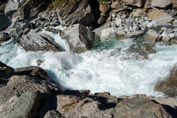 Büyük kayaların üzerinden akan ve köpüklü su oluşturan akan bir nehrin yakın çekim görüntüsü. Sahne kayalık bir arazide suyun doğal güzelliğini ve gücünü yakalar..