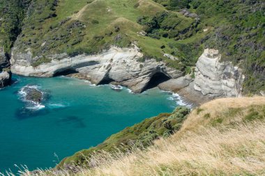 Engebeli uçurumlar, turkuaz sular ve yemyeşil sulardan oluşan manzaralı bir sahil manzarası. Manzara doğal kaya oluşumlarını ve doğa severler ve seyahat meraklıları için ideal sakin bir plaj alanını sergiliyor..