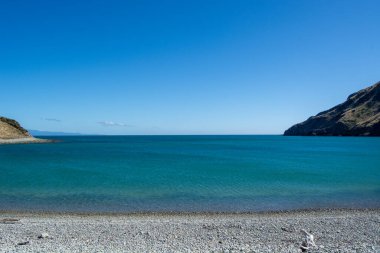 Sakin turkuaz suların, berrak mavi bir gökyüzünün ve kayalık bir kıyı şeridinin olduğu sakin bir sahil sahnesi. Manzara sakin, rahatlamak ve doğayı takdir etmek için ideal..