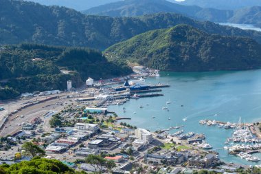Marinası olan bir sahil kasabasının havadan görünüşü, rıhtımda tekneler, ve bölgeyi çevreleyen yemyeşil tepeler. Kasaba, yoğun bir limana sahip konut ve ticari binaların bir karışımına sahip..