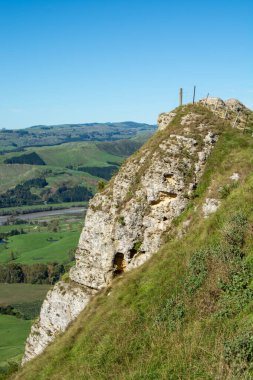 Yeşil çimenler ve çalılarla sarp kayalık bir uçurum, yemyeşil bir vadiye tepeden bakan ve açık mavi gökyüzünün altında yuvarlanan tepeler..