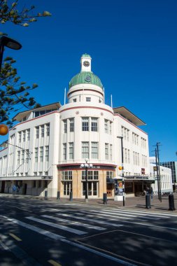 Yeşil kubbesi ve saat kulesi olan tarihi bir bina. Sanat deco mimarisi tarzında. Ön cephe beyaz, geniş pencereli, açık mavi gökyüzüne karşı kurulmuş..