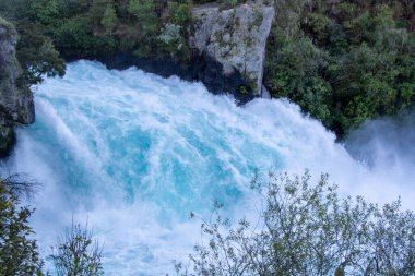 Bereketli yeşilliklerle çevrili kayalık kayalıkların üzerinde çağlayan güçlü bir şelale. Su canlı bir turkuazdır, doğal manzara ile çarpıcı bir kontrast yaratır..