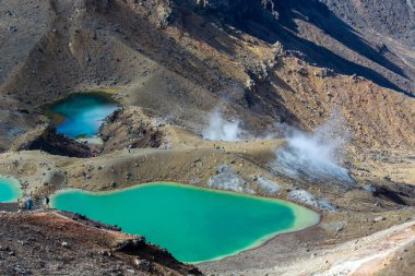 Engebeli dağlarla çevrili jeotermal göllerin çarpıcı manzarası. Turkuaz su, volkanik manzaranın toprak tonlarıyla çelişiyor. Yerden yükselen buharı gösteriyor..