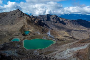 Volkanik bir alana yerleşmiş turkuaz göllü engebeli dağların nefes kesici hava manzarası. Gökyüzü parçalı bulutlu, derinlik katıyor..