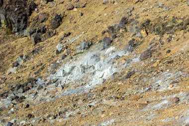 Kahverengi toprak ve dağınık taşların karışımından oluşan kayalık bir yamaçta beyaz mineral yatakları bulunur. Manzara kurak ve engebeli görünüyor. Jeolojik oluşumlar gösteriyor..
