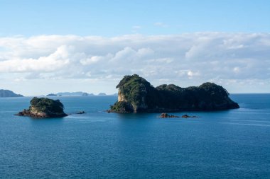 Sakin mavi sularla çevrili birkaç küçük adanın huzurlu manzarası. Dağınık bulutlarla dolu berrak bir gökyüzünün altında..