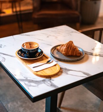 Marşmelovlu tarçınlı Latte ve Mermer Masa üzerinde kruvasan.