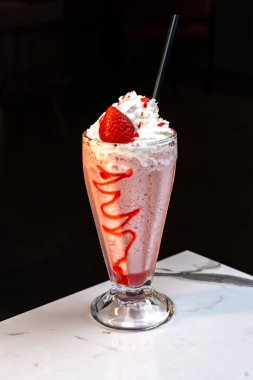 Çilekli milkshake, krem şantili ve mermer masadaki uzun camlı şuruplu.