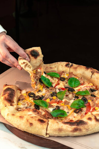 Женские руки поднимают кусочек неаполитанской пиццы на сельском столе. Момент с колбасой идеально подходит для рекламы ресторанов, меню и кулинарных блогов.