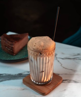 Ribbed Glass 'da kremalı buzlu Raf Coffee. Arka planda bulanık çikolatalı pasta. Kafeler, içki menüleri, sosyal medya görselleri için mükemmel.
