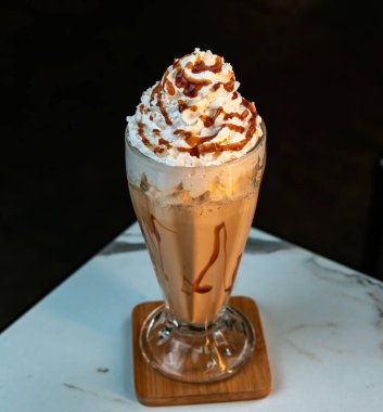 Çikolatalı milkshake, krem şantili ve uzun camlı karamel yağmurlu. Esmer arka planı olan mermer bir masada izole edilmiş. İçecek menüleri, reklamlar ve kafe markaları için ideal..