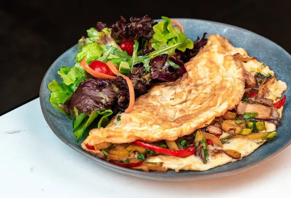 Doldurulmuş sebzeli omlet ve karışık salata. Parlak kiraz domatesleri ve renkli biberler. Sağlıklı menüler, kahvaltı, yemek blogları için mükemmel..
