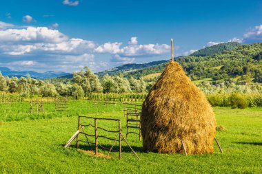 Romanya kırsalında. Kırsal Romanya manzarası, bir saman yığını, yeşil alan, dağlar ve bulutlu mavi gökyüzü. Fotoğraf Romanya 'nın kuzeyindeki Maramures bölgesinde çekildi.
