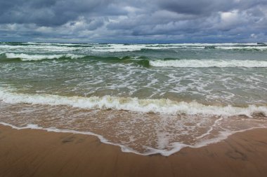 Baltık Denizi 'nin vahşi kıyıları. Kumsala gelen dalgalar, arka planda dramatik bulutlu gökyüzü. Fotoğraf Kuzey Polonya 'daki Slowinski Ulusal Parkı' nda çekildi..
