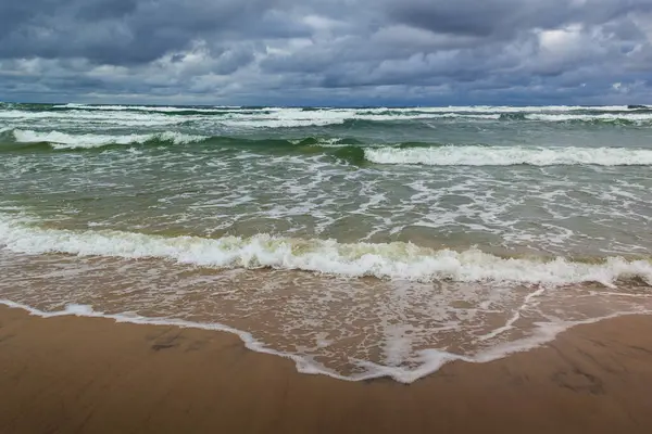 Baltık Denizi 'nin vahşi kıyıları. Kumsala gelen dalgalar, arka planda dramatik bulutlu gökyüzü. Fotoğraf Kuzey Polonya 'daki Slowinski Ulusal Parkı' nda çekildi..