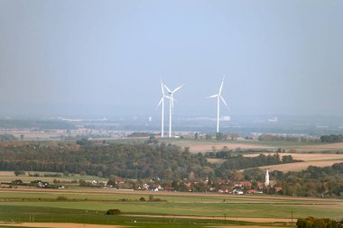 Sisli bir günde, üç rüzgar türbininin panoramik görüntüsü yenilenebilir enerji ve çevresel sürdürülebilirliği gösteriyor.