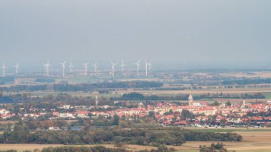 Sisli bir günde ufukta rüzgar türbinlerinin panoramik görüntüsü. Resimli bir kasaba manzarası. Yenilenebilir enerji ve çevresel sürdürülebilirlik, kırsal mimari