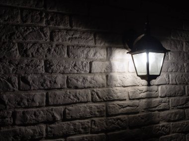 Retro-style lamp hangs on a white brick wall, copy space. Black metal wall lamp at night in the dark.