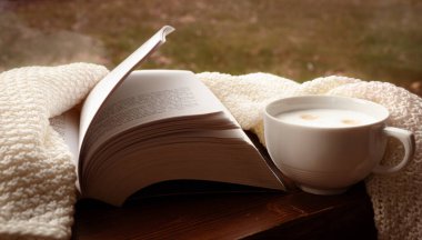 Sıcak bir fincan kahve, açık bir kitap, sonbaharda pencerenin yanında bej yumuşak battaniye. Sıcak, tatlı ev atmosferi. hygge yaşam tarzı konsepti.