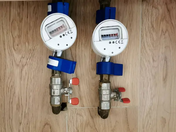 Ahşap bir yüzeyde kırmızı valf saplı iki su ölçer boru hattına yerleştirildi. Su tüketimi izleme, tesisat sistemleri, hijyenik ekipman, elektrik faturaları konsepti