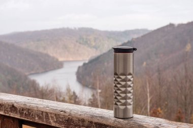 Çelik termos, bir fincan sıcak çay ya da tepelere ve göle karşı ahşap balyaların üzerinde kahve. Sonbaharda dağlarda piknik. Seyahat konsepti. Sıfır atık, plastiksiz. Boşluğu kopyala