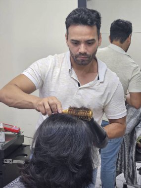 Odaklanmış bir kuaför, müşterinin saçını modern bir güzellik salonunda saç kurutma makinesi ve saç fırçası kullanarak şekillendirir. Kuaför, stil sahibi ve sofistike bir görünüm yaratarak saçı şekillendirirken yetenek ve adanmışlık gösteriyor. Salonun ambiyansı... 