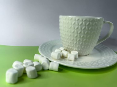 Beyaz marşmelovlar kahve fincanının yanındaki parlak yeşil arka plana saçılmış. Kopyalama alanı olan minimalist yemek kompozisyonu. Atıştırmalık, tatlı, tatlı ya da yemek dokusu. Yüksek kalite fotoğraf