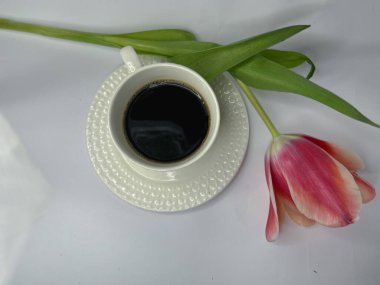 Beyaz arka planda bir fincan kahve, dizüstü bilgisayar, turuncu-pembe lale tomurcuğu, sabah bahar atmosferi. Yüksek kalite fotoğraf