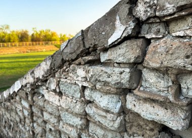 Eski, dokulu tuğlaları olan taştan bir duvara yakın plan. Yüzeyde doğal aşınma ve çatlaklar, tasarım projelerinde grunge arkaplan veya yapı dokusu olarak kullanılmak için idealdir. Yüksek kalite