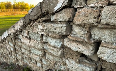 Eski, dokulu tuğlaları olan taştan bir duvara yakın plan. Yüzeyde doğal aşınma ve çatlaklar, tasarım projelerinde grunge arkaplan veya yapı dokusu olarak kullanılmak için idealdir. Yüksek kalite