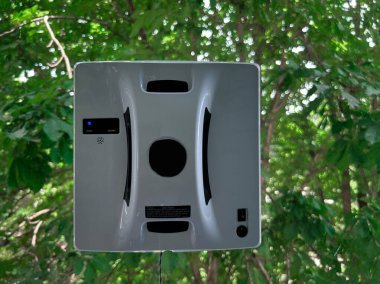 Arka planda yeşil ağaçlar olan cam camlar üzerinde çalışan akıllı cam temizleme robotu. Ev bakımı ve akıllı yaşam için modern otomatik temizleme cihazı. Yüksek kalite fotoğraf