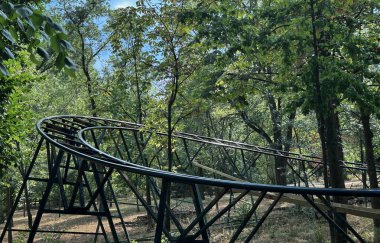 Ormanda yeşil ağaçlarla çevrili terk edilmiş lunapark treni rayları. Unutulmuş eğlence parkı, çürüme, doğa ıslah yapıları ve şehir keşfi kavramı. Yüksek kalite fotoğraf