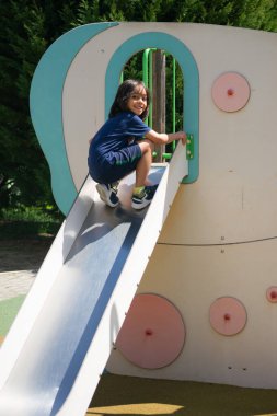 Güneşli bir yaz gününde çocuk parkında kayak yaparken eğlenen genç bir çocuk.
