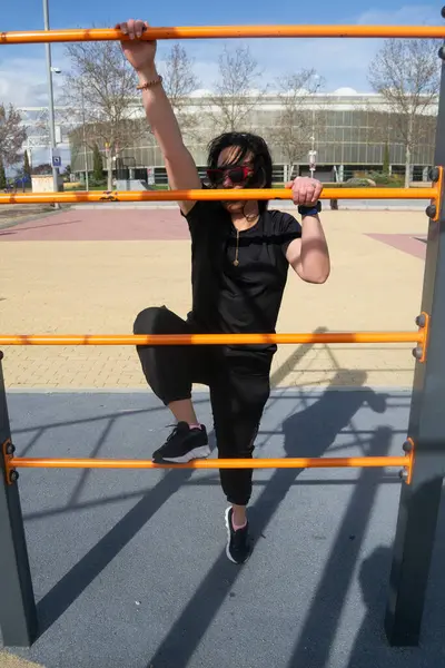 Sporcu kadın jimnastik parkında turuncu paralel parmaklıklara tırmanıyor.