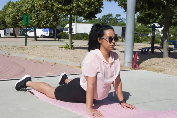 Sportif kadın, yukarı bakan köpek pozu veriyor. Spor minderinde poz veriyor. Şehir parkında spor yapıyor.