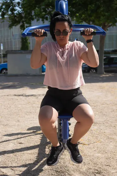 Azimli bir kadın sokak çalışma makinesinde ağırlık kaldırıyor, sağlıklı yaşam tarzını ve uygunluğunu destekliyor.