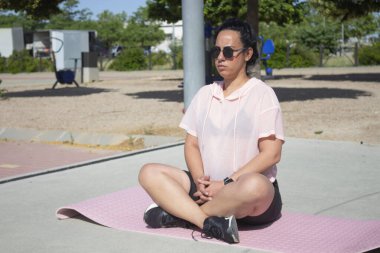 Nilüfer pozisyonunda yoga yapan kıvrımlı bir kadın. Şehir parkında pembe bir paspas üzerinde.