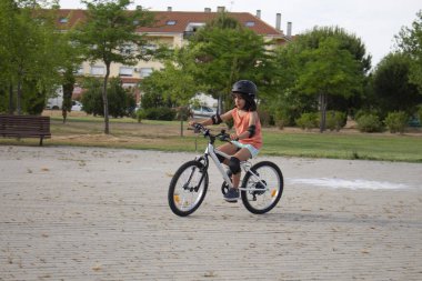 Şehir parkında kask takıp bisiklet sürmeyi öğrenen bir kız.