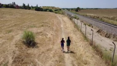 Güneşli bir günde kırsalda bir demiryolunun yanında koşan iki sporcu