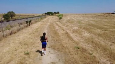 Kırsal kesimdeki bir demiryolunun yakınındaki toprak yolda koşan bir sporcu.