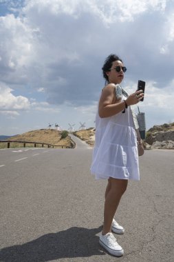 Akıllı telefon kullanan kadın yaz tatillerinde Consuegra, Toledo, İspanya 'da yel değirmenlerinin fotoğraflarını çekiyor.