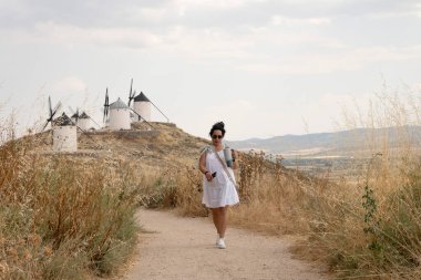 İspanya 'nın Toledo eyaletindeki tarihi yel değirmenlerine doğru yürüyen kadın turist yaz tatillerinin tadını çıkarıyor.