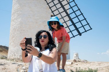 Yaz tatillerinde İspanya 'nın Campo de Criptana kentinde geleneksel beyaz yel değirmenleri önünde akıllı telefon ile selfie çeken turistler