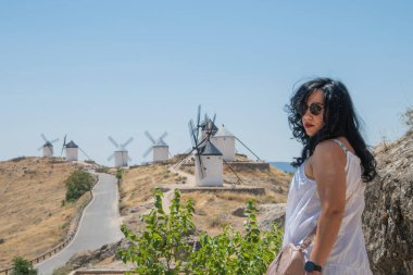 Konsuegra, Kastilya, La Mancha 'da güneşli bir yaz gününde ünlü rüzgar değirmenlerine doğru yürüyen turistler.