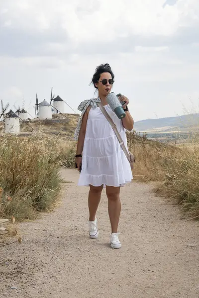Arka planda yel değirmenleri olan bir yolda yürüyen kadın.