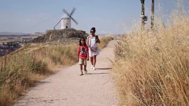 Kadın ve kız Consuegra, İspanya 'nın yel değirmenleri yakınlarında yürüyorlar.