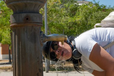 Sıcak bir yaz gününde halka açık bir çeşmeden su içen bir turist.